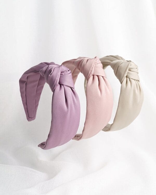 Kolme satiinista hiuspantaa solmulla vierekkäin