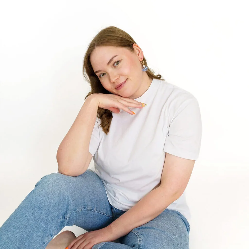 Kuvassa nainen istuu lattialla ja katsoo kameraan