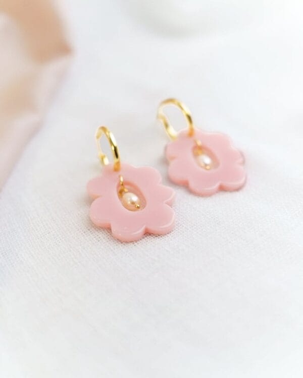 Lähikuva kukan muotoisista vaaleanpunaisista korvakoruista helmellä ja kultaisilla korvakorurenkailla