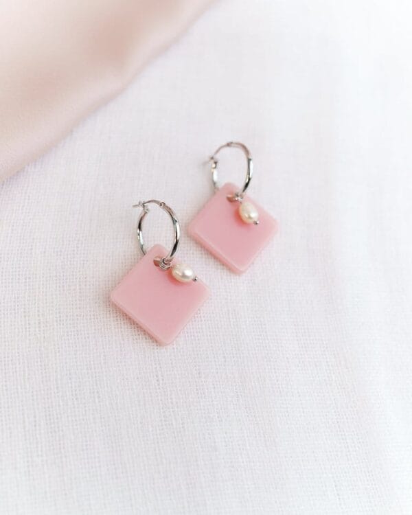 Neliön muotoiset korvakorut helmellä ja hopeisilla korvakorurenkailla vaaleaa taustaa vasten