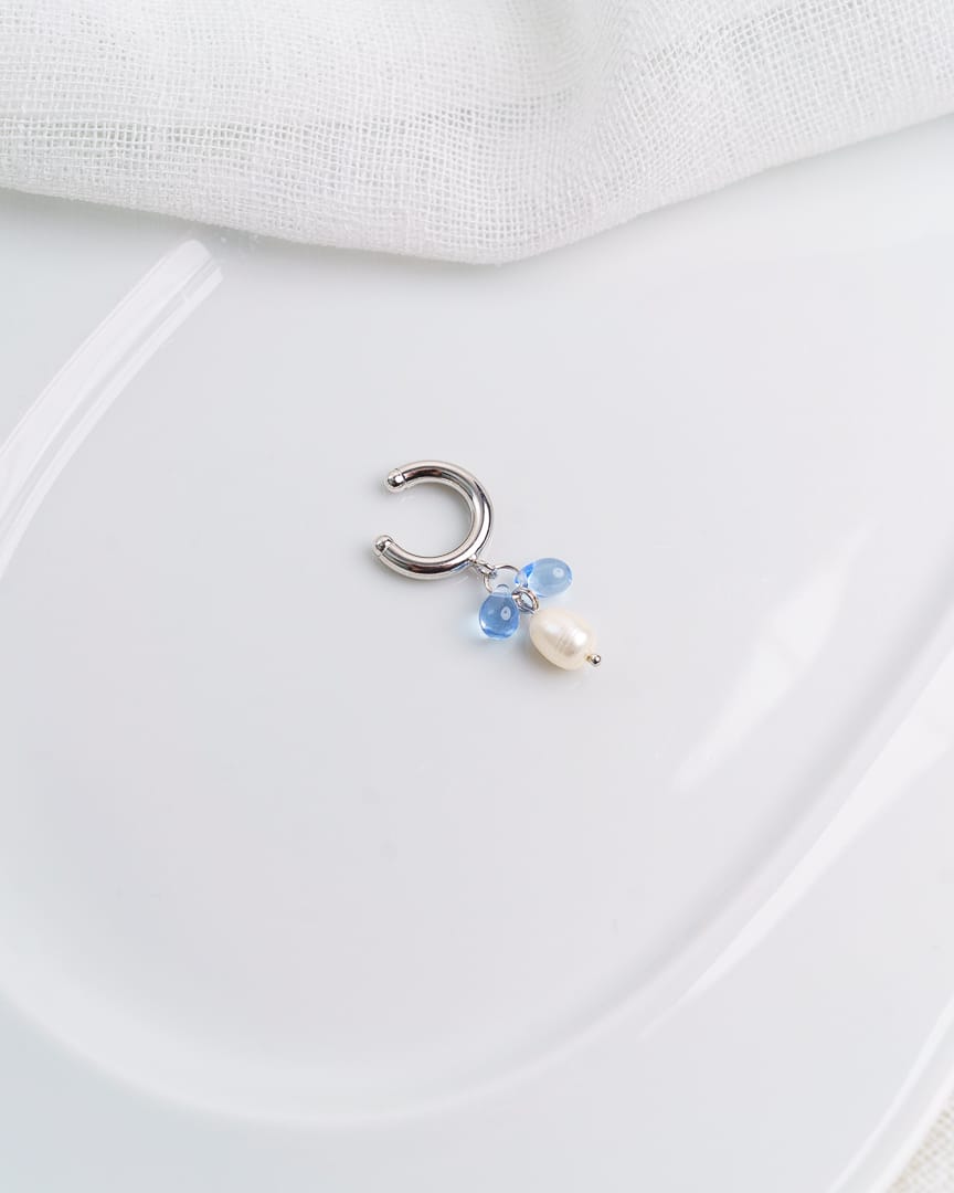 Kuvassa vaalealla taustalla valkoinen astia, jonka päälle aseteltu earcuff korvakoru.