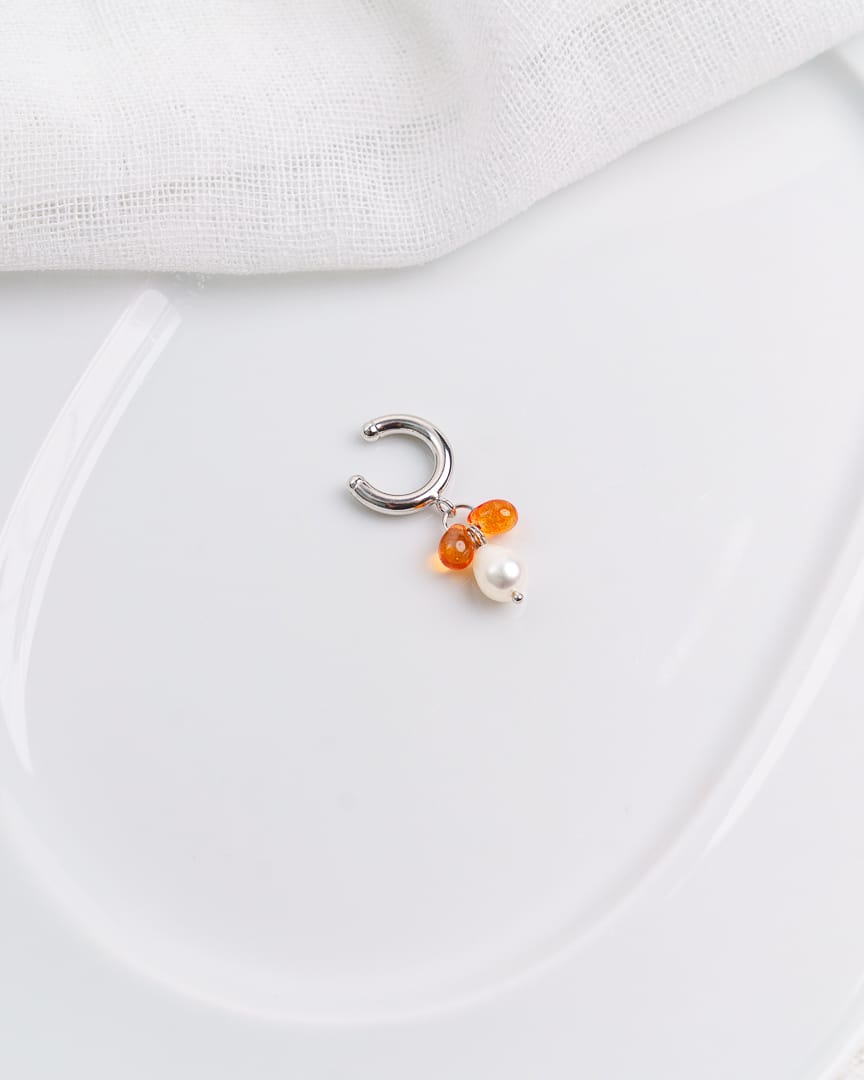 Kuvassa vaalealla taustalla valkoinen astia, jonka päälle aseteltu earcuff korvakoru.