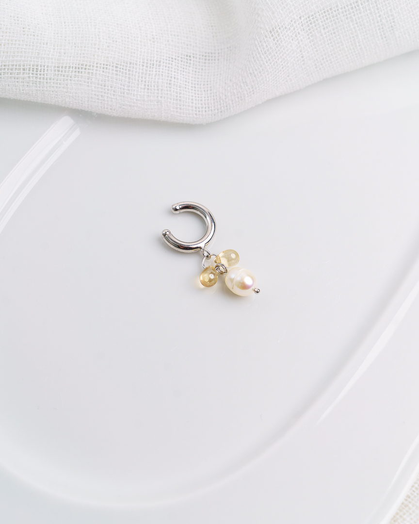 Kuvassa vaalealla taustalla valkoinen astia, jonka päälle aseteltu earcuff korvakoru.
