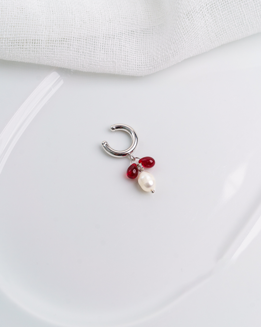 Kuvassa vaalealla taustalla valkoinen astia, jonka päälle aseteltu earcuff korvakoru.