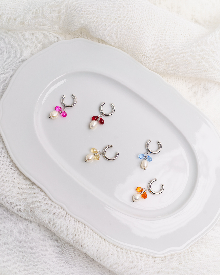 Kuvassa vaalealla taustalla valkoinen astia, jonka päälle aseteltu earcuff korvakoruja.